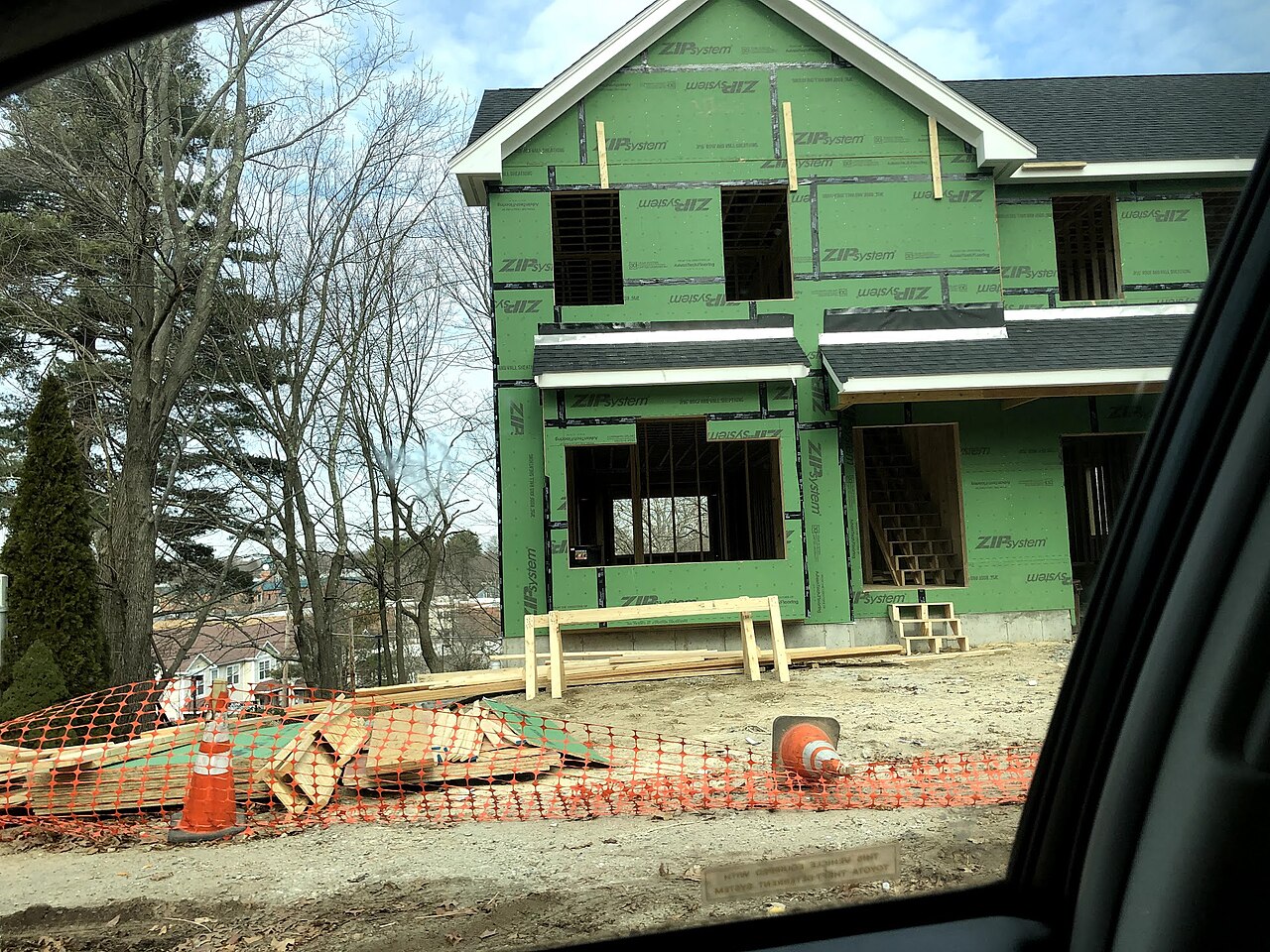 Wood framing and sheathing on a single-family house under construction, seen from the street.