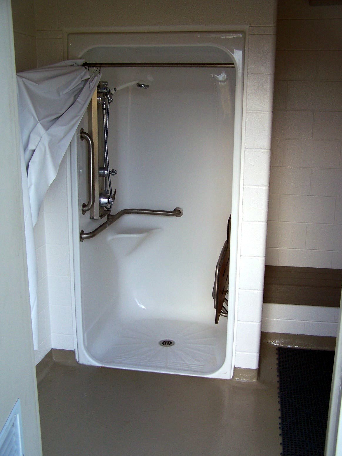 An accessible shower stall with wall-mounted grab bars, a handheld showerhead, a built-in seat, and a nonslip floor surface.