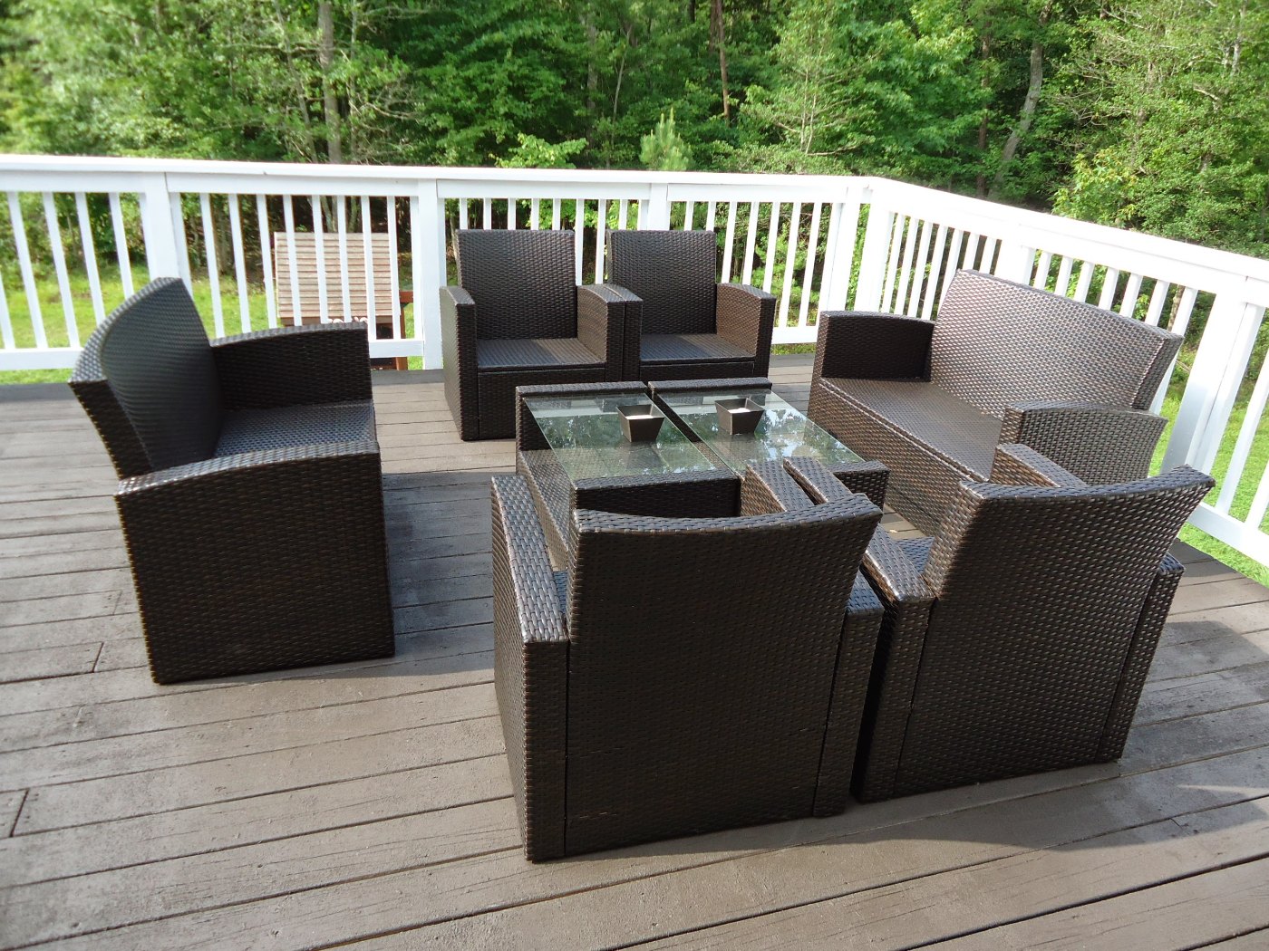 Outdoor wood deck with railing and patio furniture beside mature trees.