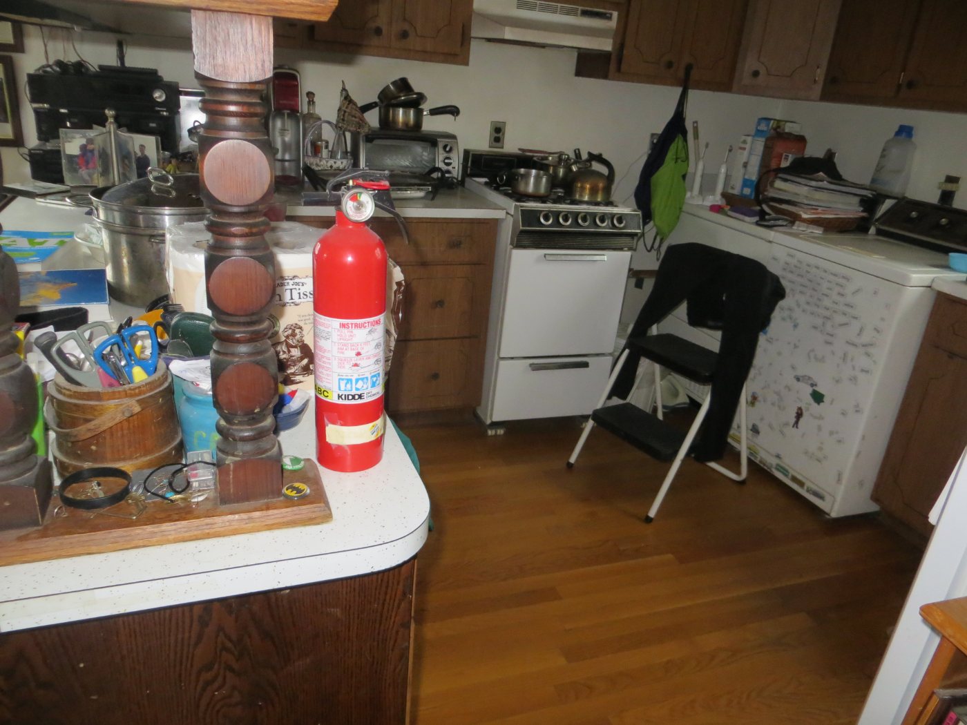 A red fire extinguisher sits on a counter in a residential kitchen beside a stove and refrigerator.