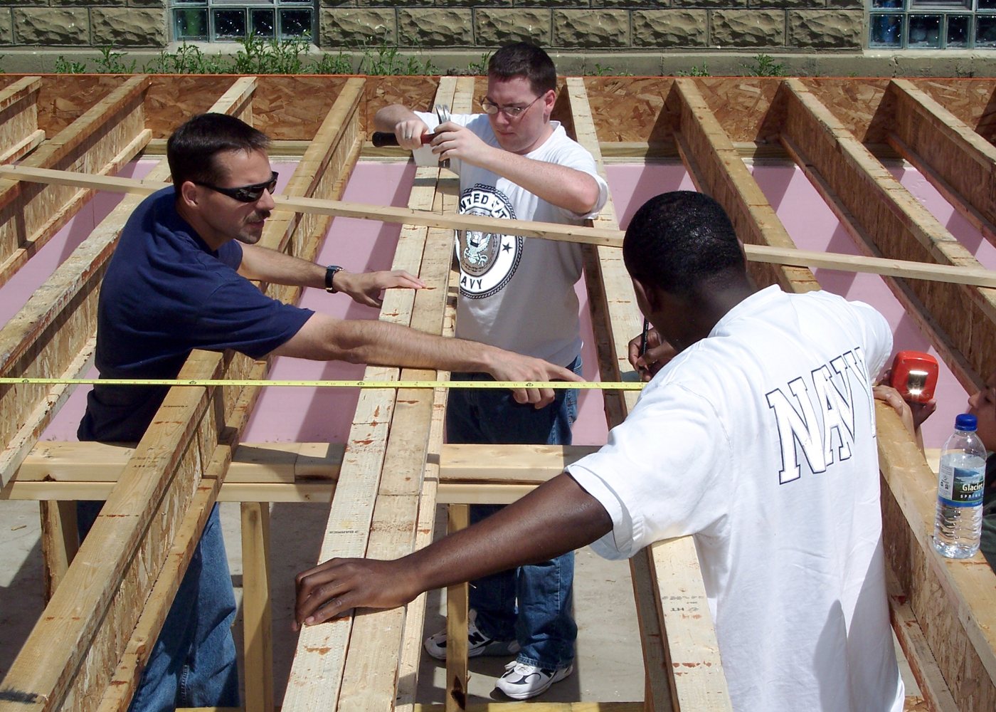 Three people measure and work on wooden floor joists during construction of a house in Harvey, Illinois.