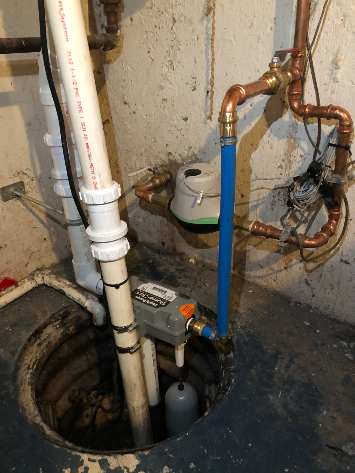 Residential basement sump pit with a submersible pump, discharge piping, and water-level float.