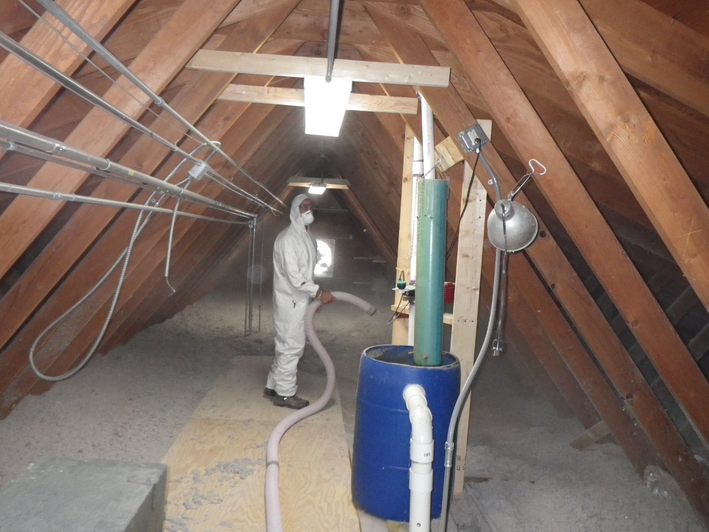 Worker wearing protective clothing installing loose-fill insulation in an attic.