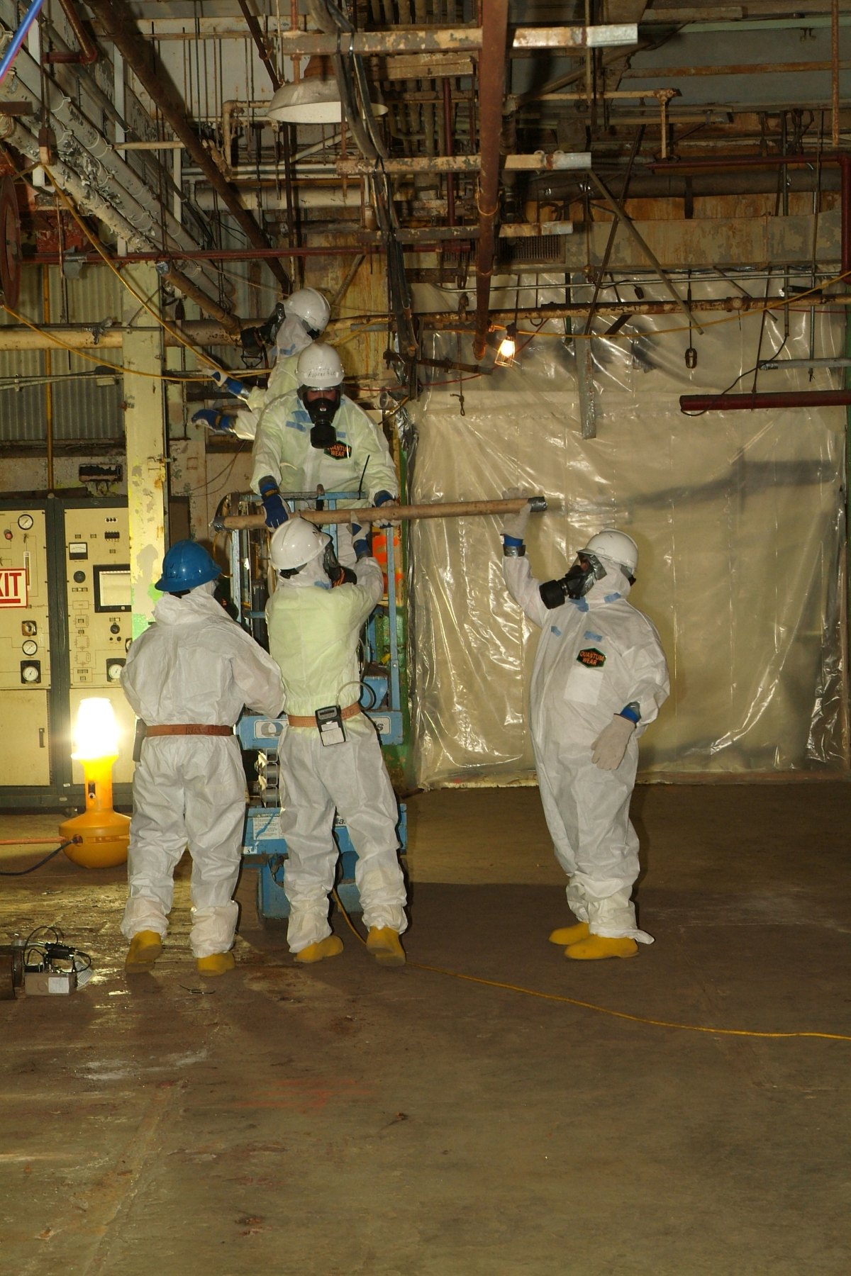 Workers in full protective suits and respirators performing asbestos-removal work inside an industrial plant.