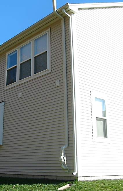 White PVC radon mitigation pipe and fan attached to the exterior wall of a Connecticut home.