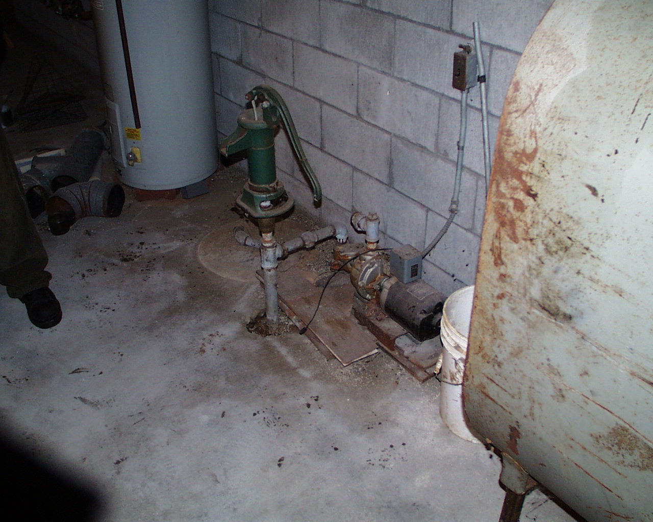 Interior residential utility area showing private water-well equipment and piping beside a large oil tank.