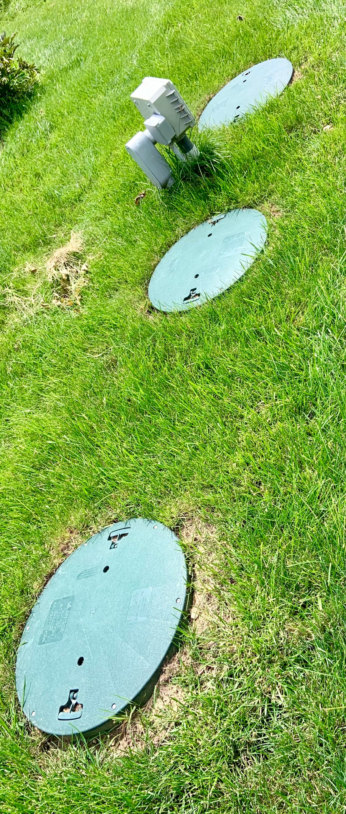 Several green septic access covers and risers arranged in a maintained Upper Midwest lawn.