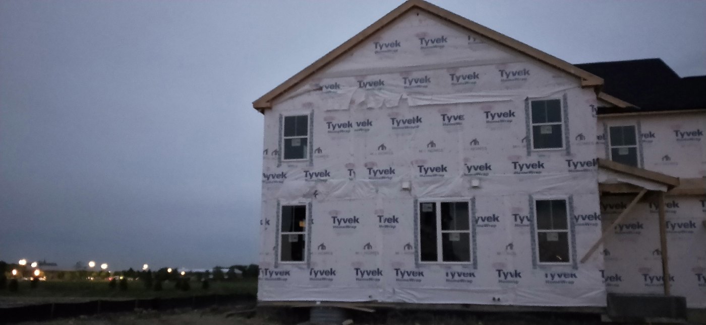 Two-story townhome under construction with white house wrap over the exterior walls in Aurora, Illinois.